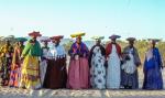 Namibialaisia naisia rivissä aurinkoisena päivänä ulkosalla pukeutuneina värikkäisiin perinneasuihin.