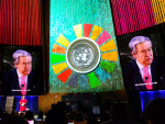 YK:n pääsihteeri Guterres kahdella suurella näytöllä kokoussalin edessä, keskellä SDG tunnus