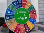jättimäinen pyöreä kestävän kehityksen tavoitteiden kuvake, jonka keskiössä terveystavoitteen vihreä sydämenrytmiä kuvaava logo