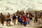 Kurdisiirtolaisia kävelemässä hiekkatiellä talvella. Vuorimaisema taustalla.