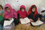 Kolme tyttöä istuu ja lukee oppikirjaa telttakoulussa Afganistanissa