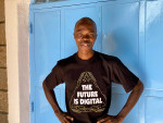 Nuori afrikkalainen mies seisoo sinisen seinän edustalla ja katsoo hymyillen kameraan. Hänellä on t-paita, jossa lukee "The Future is Digital". 