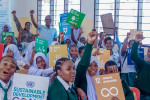 Tansanialaisia koululaisia innokkaasti pitelemässä kestävän kehityksen tavoitteiden kuvakkeita.