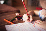 Lapsi kirjoittaa, kädessä punainen kynä